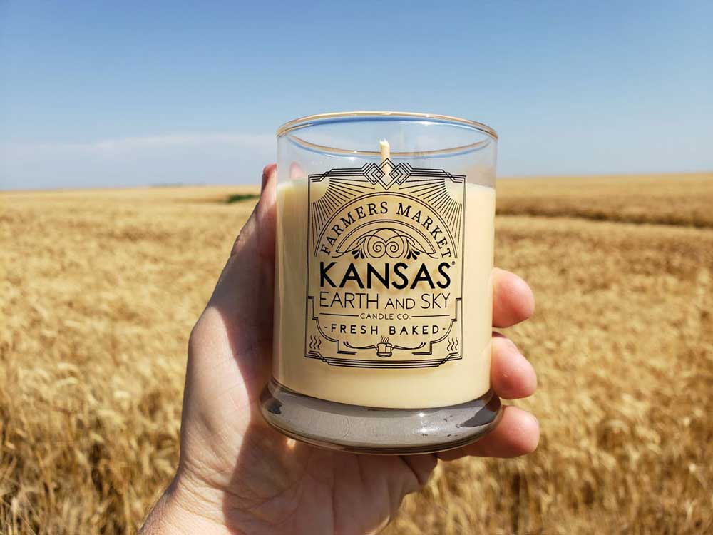 A Kansas Earth and Sky candle being held in front of a wheat field